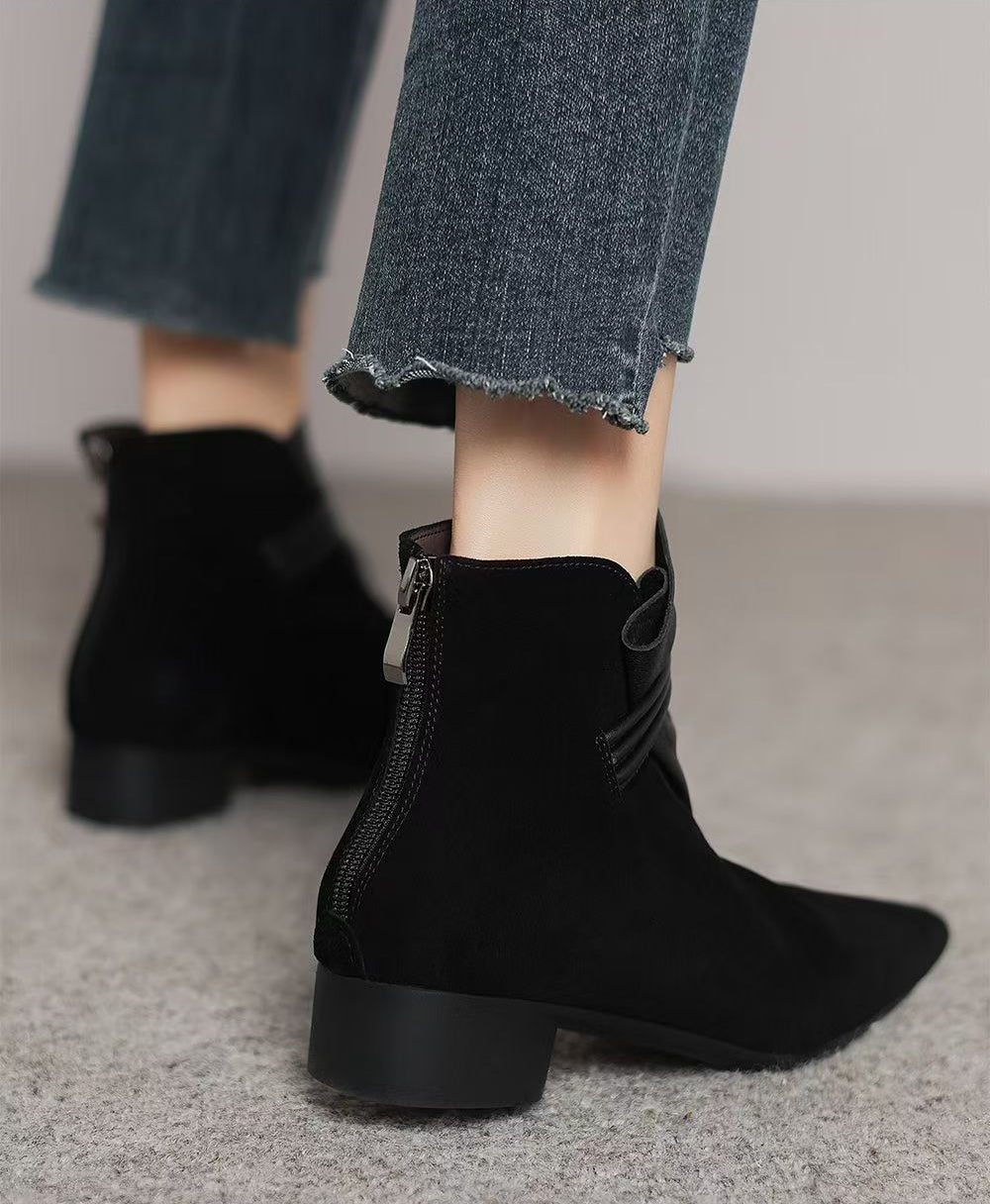 Black suede ankle boots with a side zipper and bow detail, shown on a model wearing frayed blue jeans.