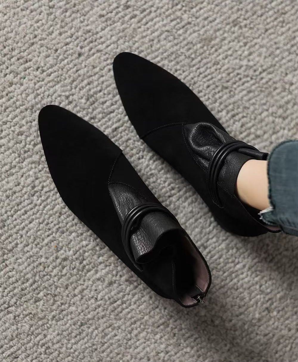 A pair of black pointed-toe ankle boots with a textured faux-leather finish, shown on a gray carpeted floor with a person's foot wearing one boot. Text at the top reads 'Enjoy a comfortable life'.