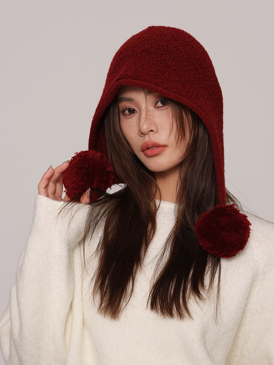 Margo & Main red wool pom pom hood — three-quarter view with one pom pom held out