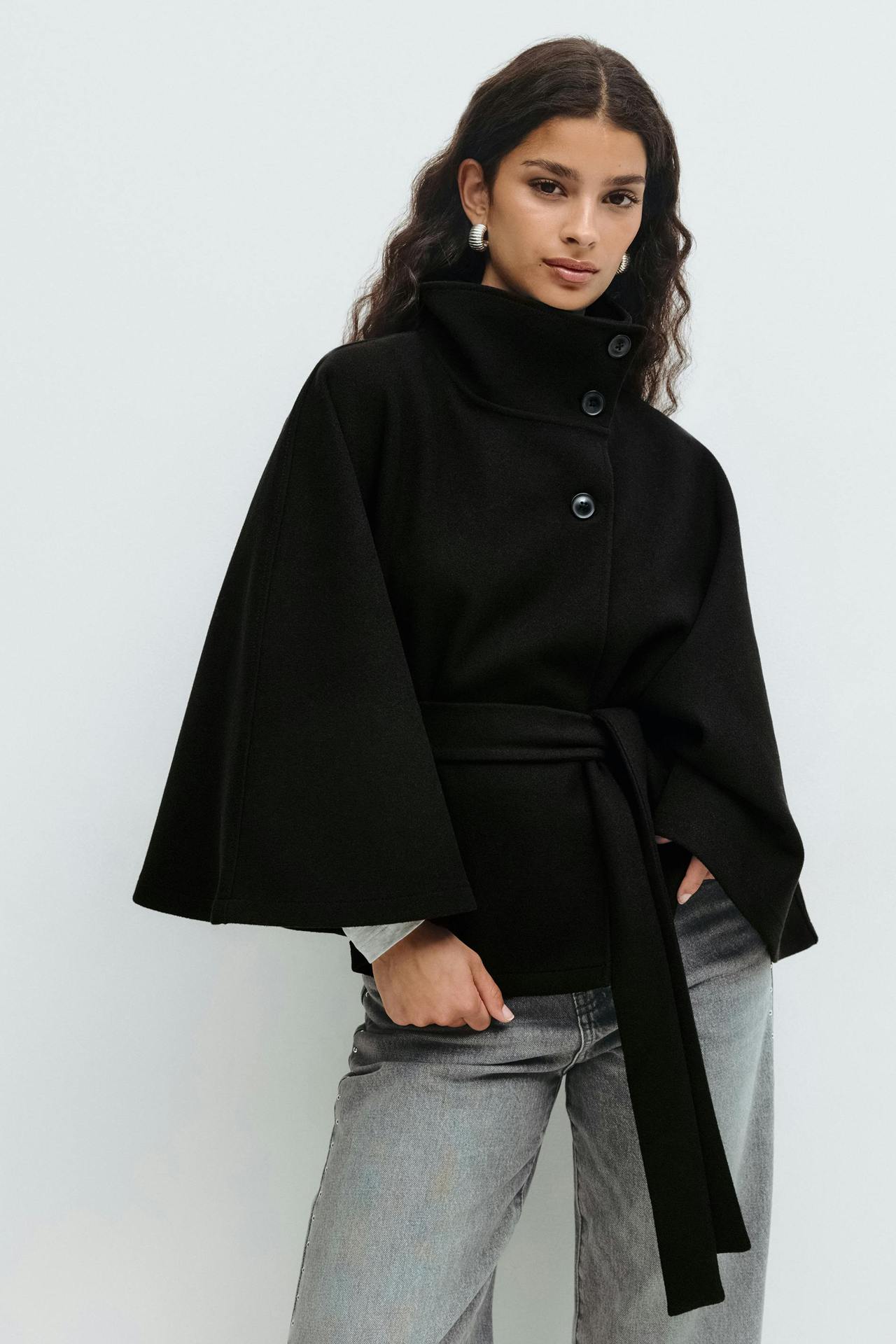 Margo & Main – Anneke black button-front belted cape coat, waist-up front view with grey jeans, US women's sizes