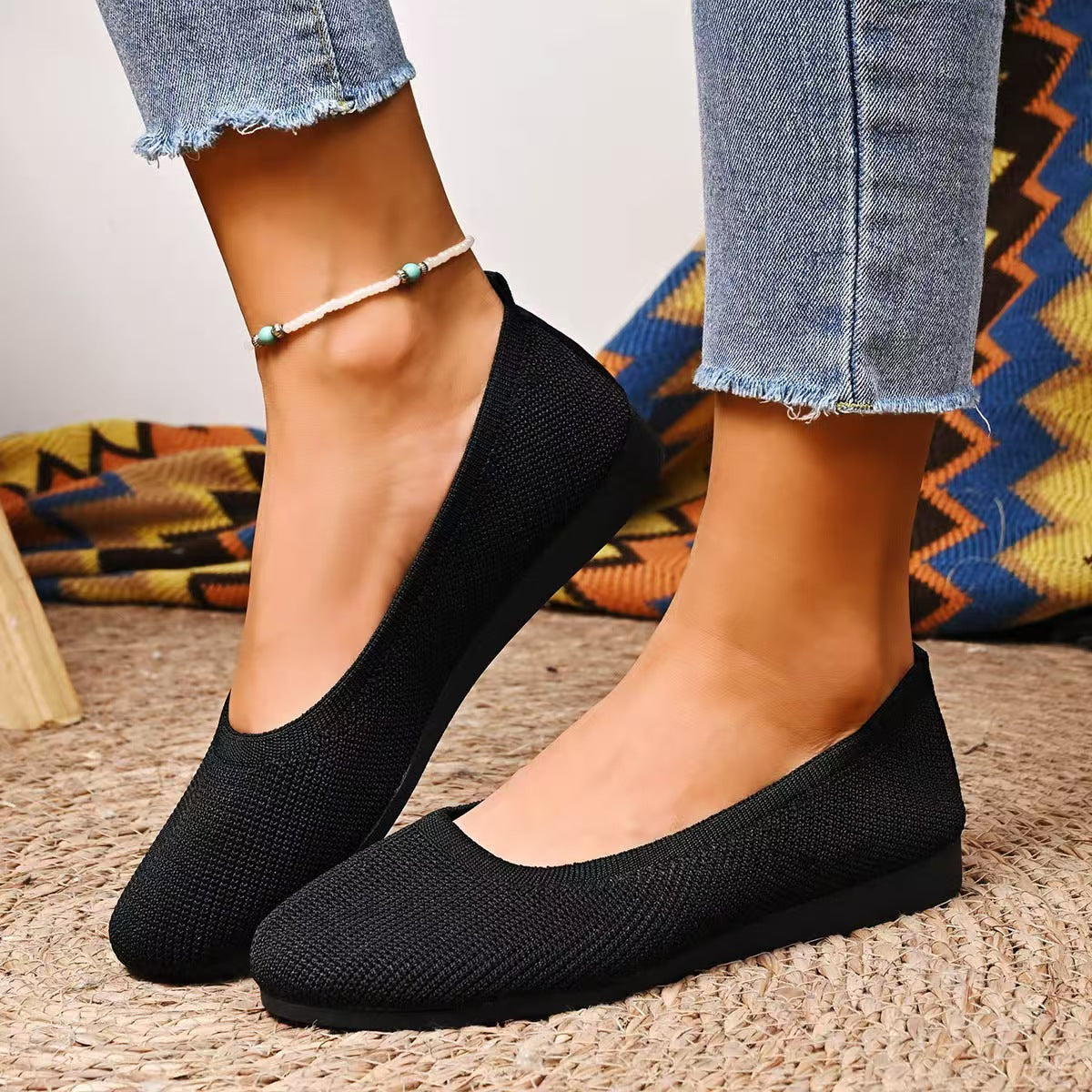 Margo & Main – Astri black knit slip-on comfort ballet flats, worn front view with cropped jeans on a woven rug, US women's sizes